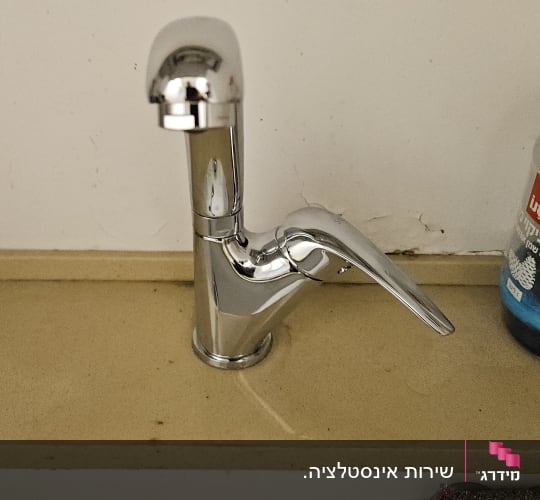 ברז מים מניקל מבריק המותקן על משטח מעל כיור